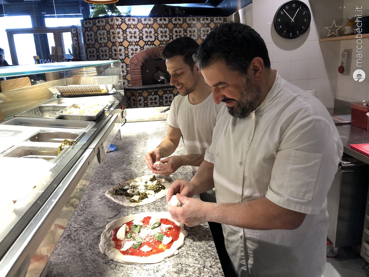 Michele Leo e il suo aiutante aggiungono la mozzarella sulle pizze rompendola con le mani