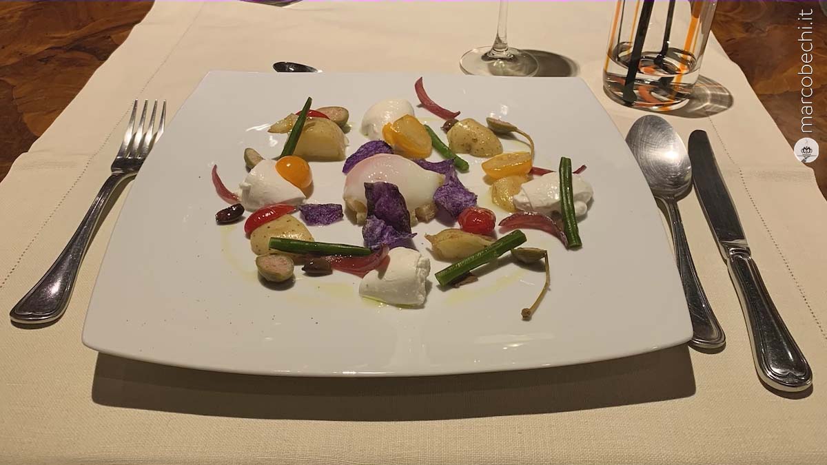 Insalata Nizzarda Le Contrade con mozzarella di bufala, patate novelle, pomodoro, olive taggiasche, cipolla in agrodolce, uovo a bassa temperatura su crostino di pane, fagiolini e fiori di cappero