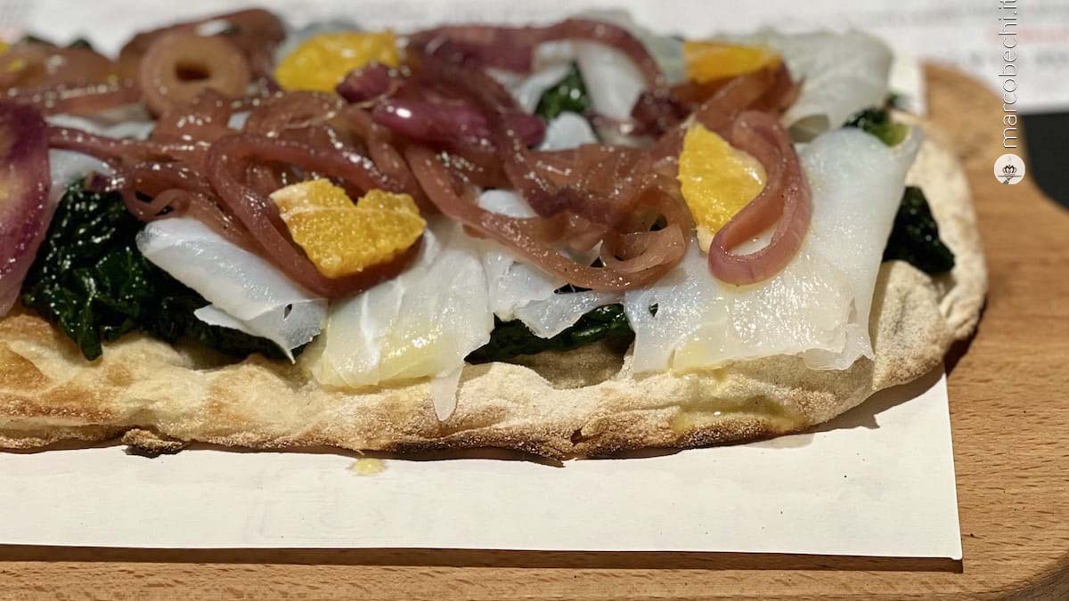 Stella, una pinsa con carpaccio di baccalà, cipolla caramellata e cavolo nero.